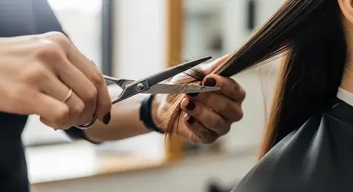 Un coiffeur coupant une mèche de cheveux longs et bruns avec des ciseaux de coiffure dans un salon.